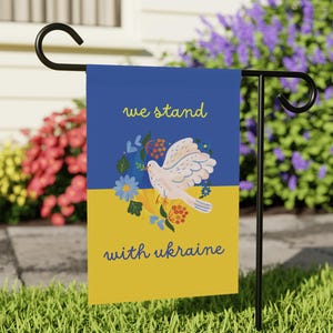 May include: A blue and yellow garden flag with a white dove and flowers. The flag reads "we stand with ukraine".