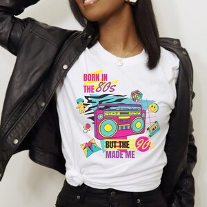 May include: White t-shirt with a graphic design featuring a boombox, a smiley face, a Rubik's cube, and the text "Born in the 80s but the 90s made me".