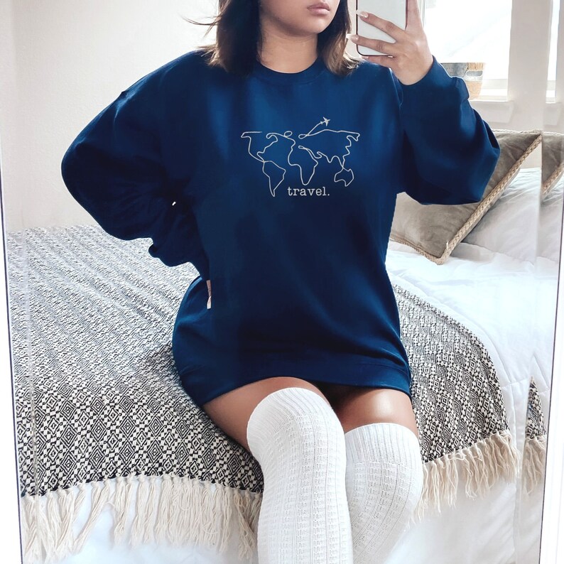 Puede incluir: Sudadera azul marino con un contorno blanco de un mapa del mundo y un avi&oacute;n. La palabra "travel" est&aacute; impresa debajo del mapa. La sudadera es de manga larga y tiene cuello redondo.