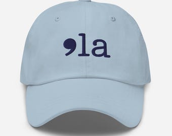 May include: A light blue baseball cap with a navy blue embroidered semicolon and the word "la" on the front.