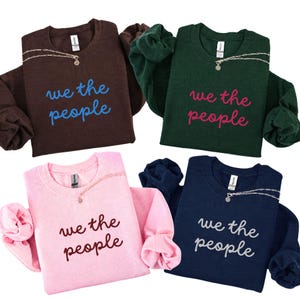 Può includere: Quattro felpe girocollo in marrone, verde scuro, rosa chiaro e blu navy. Ognuna presenta la scritta "we the people" in un colore a contrasto e una catenina color argento drappeggiata attorno alla zona del colletto del capo.
