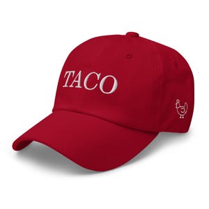 May include: A red baseball cap with the word "TACO" embroidered in white on the front. A white chicken graphic is on the side. The cap has a curved brim and a fabric strap closure.