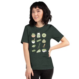 以下が含まれることがあります： 抹茶をテーマにした様々なアイテムが描かれたダークグリーンのTシャツ。抹茶のカップ、抹茶ケーキ、抹茶アイス、抹茶の泡立て器などがあります。