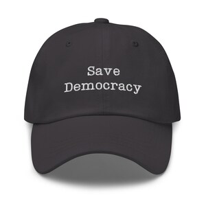 May include: A dark gray baseball cap with the text "Save Democracy" embroidered in white on the front.