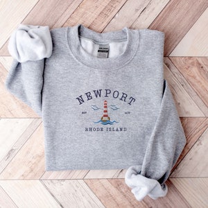 May include: Gray sweatshirt with a graphic design of a lighthouse and the text "NEWPORT" with the words "RHODE ISLAND" below it. The graphic also includes the text "EST 1639".