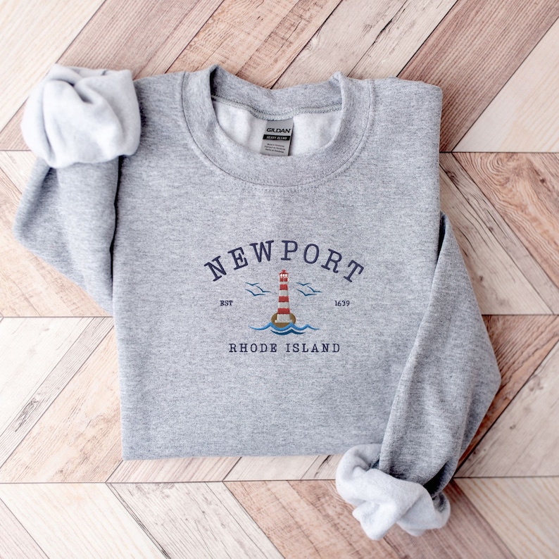 May include: Gray sweatshirt with a graphic design of a lighthouse and the text "NEWPORT" with the words "RHODE ISLAND" below it. The graphic also includes the text "EST 1639".