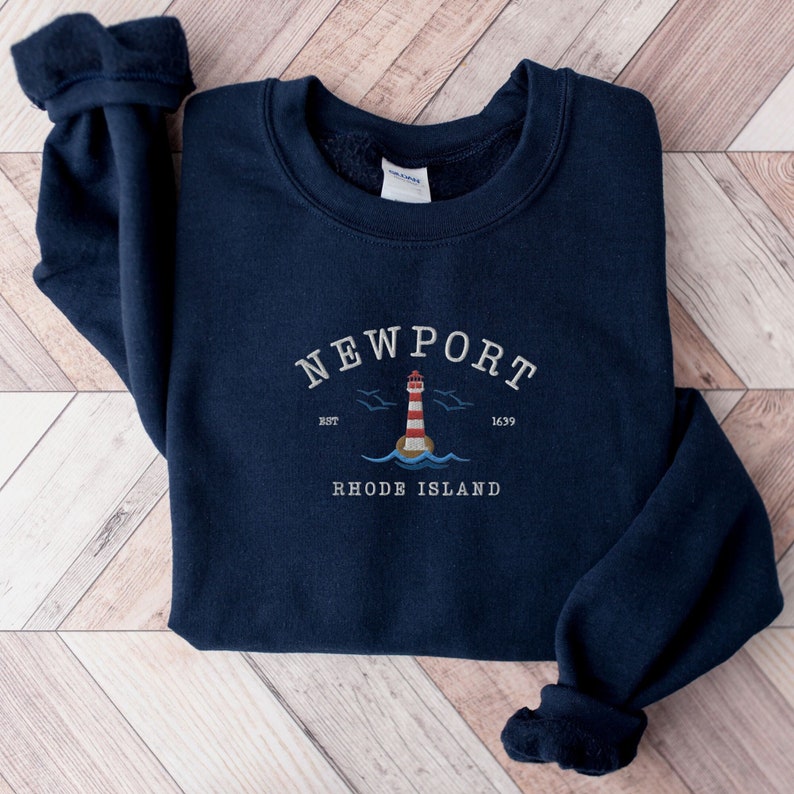 May include: Navy blue sweatshirt with a white embroidered design featuring a lighthouse, birds, and the text "NEWPORT EST 1639 RHODE ISLAND".