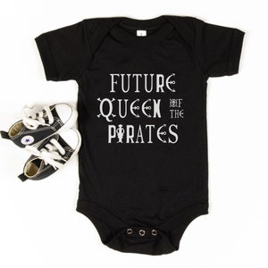 May include: Black baby onesie with white text that reads "FUTURE QUEEN OF THE PIRATES". The text is stylized with nautical symbols.