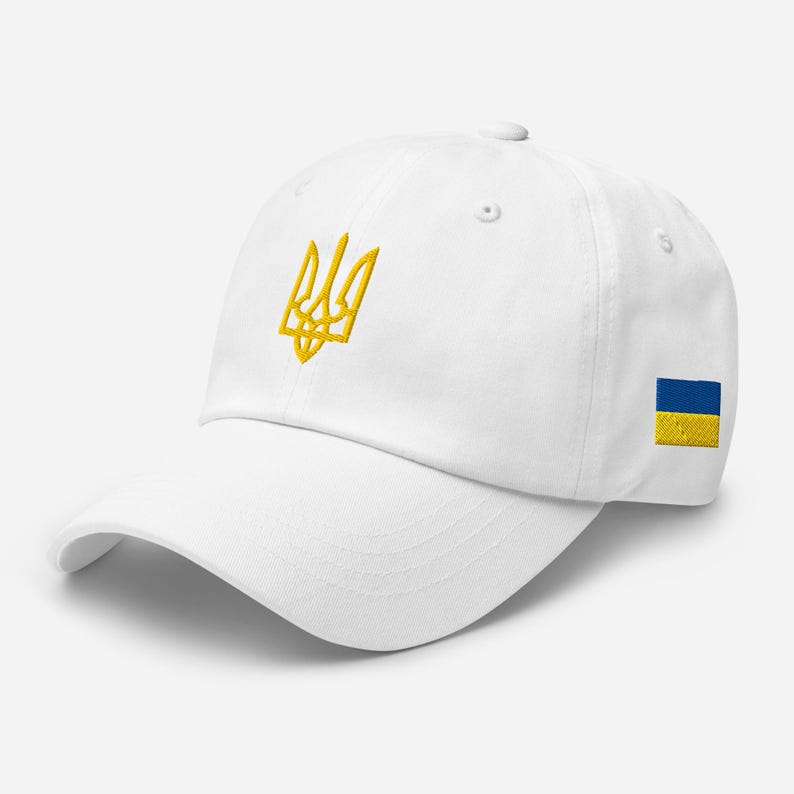 May include: White baseball cap with a yellow embroidered Ukrainian trident and a small blue and yellow Ukrainian flag patch on the side.