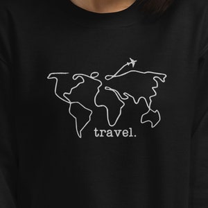 Puede incluir: Sudadera negra con un dise&ntilde;o de mapa del mundo bordado en blanco y un peque&ntilde;o avi&oacute;n. La palabra "travel." est&aacute; bordada debajo. Un dise&ntilde;o sencillo para los amantes de los viajes.
