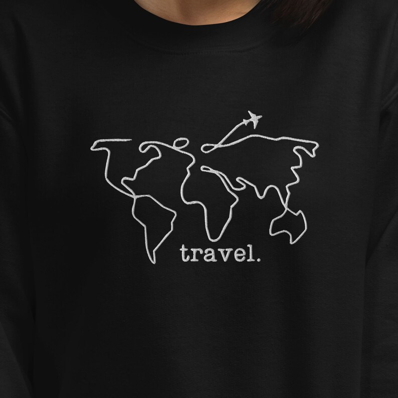Puede incluir: Sudadera negra con un dise&ntilde;o de mapa del mundo bordado en blanco y un peque&ntilde;o avi&oacute;n. La palabra "travel." est&aacute; bordada debajo. Un dise&ntilde;o sencillo para los amantes de los viajes.