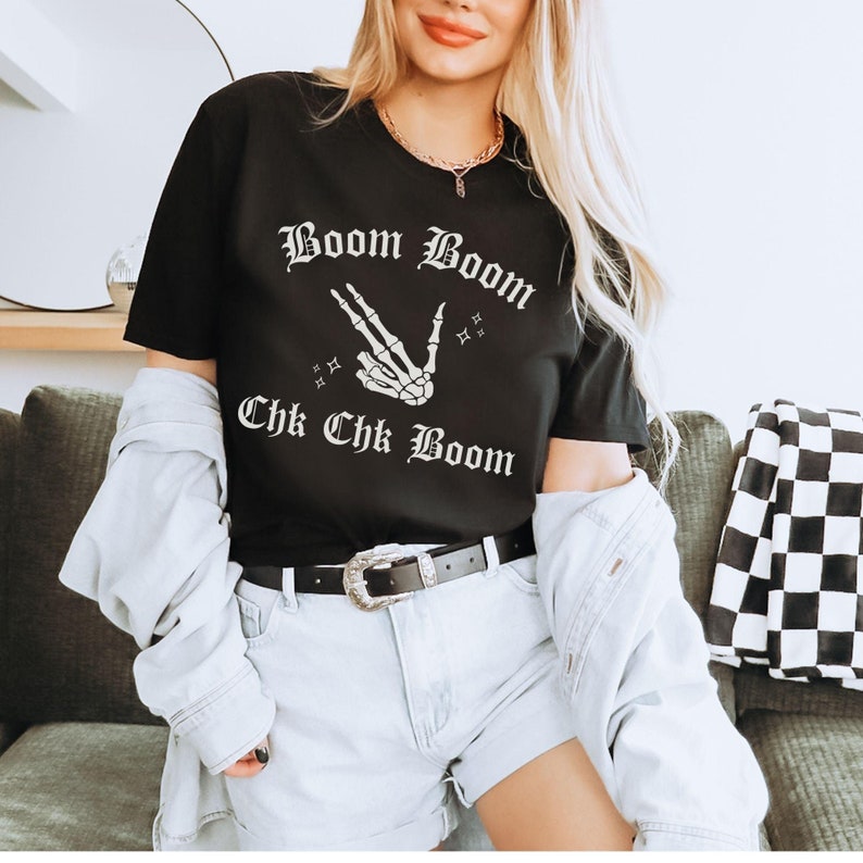 May include: Black t-shirt with a white skeleton hand making a peace sign and the text "Boom Boom Chk Chk Boom" in a gothic font.