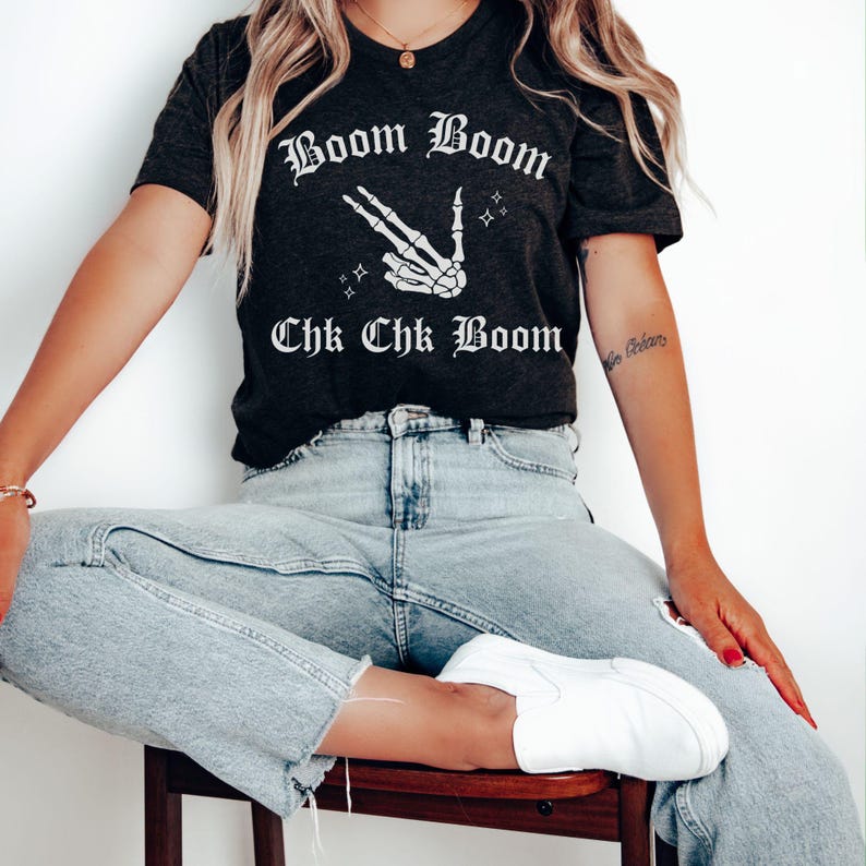 May include: A dark grey t-shirt with a white skeleton hand making a peace sign and the text "Boom Boom Chk Chk Boom" in a gothic font.