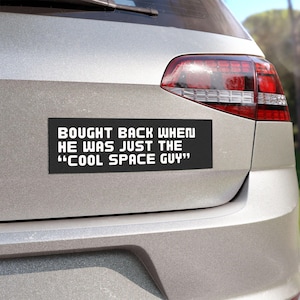 May include: A black bumper sticker with white text that reads "Bought back when he was just the "Cool Space Guy""