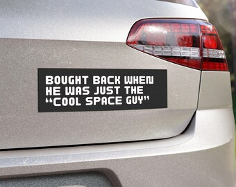 May include: A black bumper sticker with white text that reads "Bought back when he was just the "Cool Space Guy""