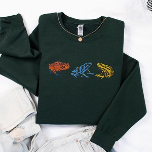 May include: A dark green sweatshirt with a row of three embroidered frogs in different colors: orange, blue, and yellow.