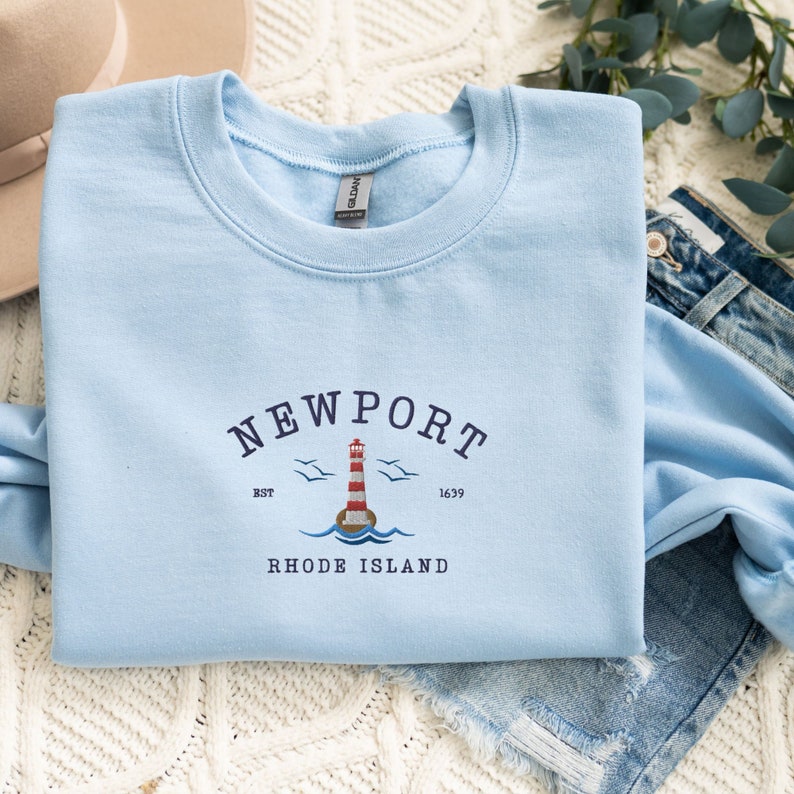 May include: Light blue sweatshirt with a white lighthouse graphic and the text "NEWPORT EST 1639 RHODE ISLAND".