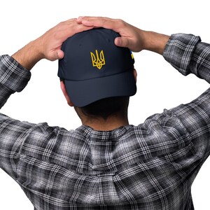 May include: A navy blue baseball cap with a yellow embroidered Ukrainian trident symbol.