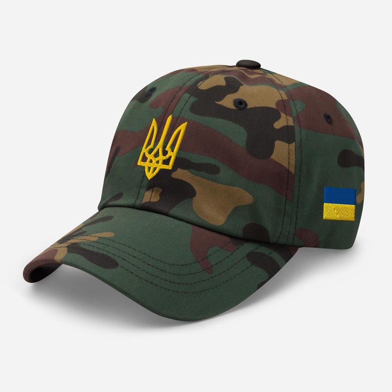 May include: A camouflage baseball cap with a yellow embroidered Ukrainian trident and a small blue and yellow Ukrainian flag patch.