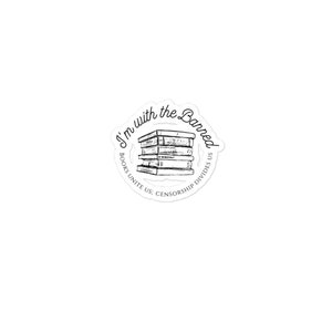 Pode incluir: Um adesivo preto e branco com o texto "I'm with the Banned" em um c&iacute;rculo. O texto "Books Unite Us: Censorship Divides Us" tamb&eacute;m est&aacute; no c&iacute;rculo. Uma pilha de livros est&aacute; no centro do c&iacute;rculo.