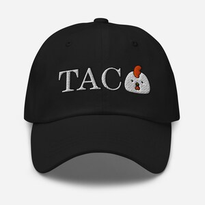 May include: Black baseball cap with the word "TACO" embroidered in white, with a cartoon chicken graphic. The cap has a curved brim and a button on top.