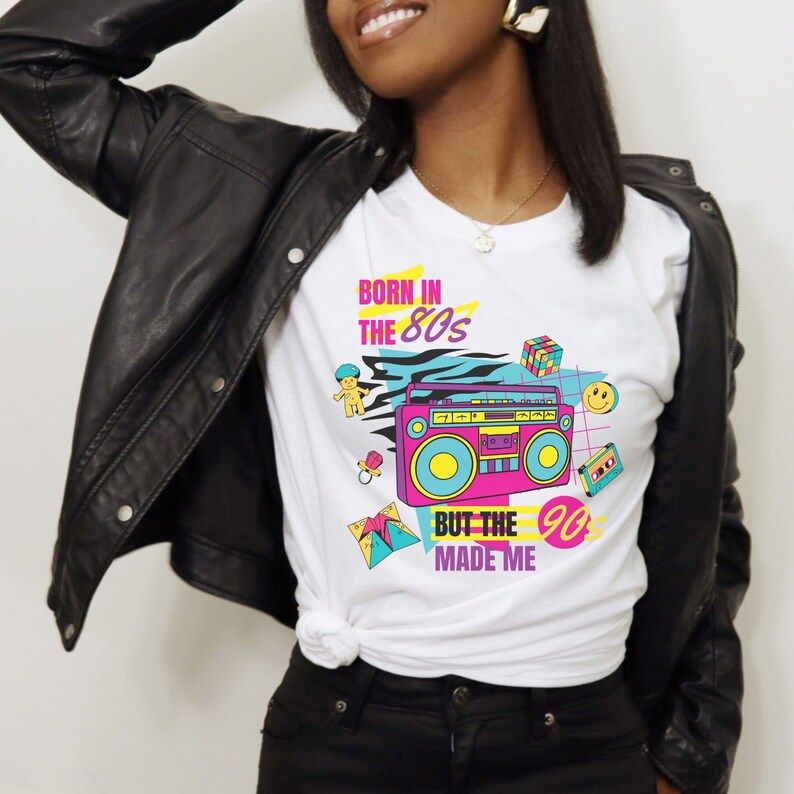 May include: White t-shirt with a graphic design featuring a boombox, a smiley face, a Rubik's cube, and the text "Born in the 80s but the 90s made me".
