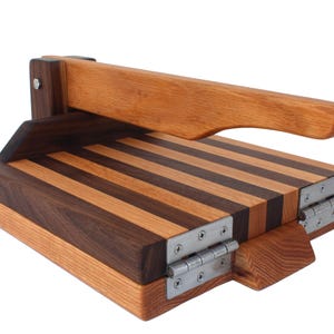 May include: A wooden press with a striped top and a hinged handle. The press is made of light and dark wood and has metal hinges.