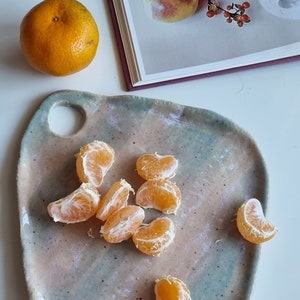 Puede incluir: Un plato de servir de cerámica azul claro y rosa con un agujero en el centro. El plato está lleno de segmentos de mandarinas peladas.