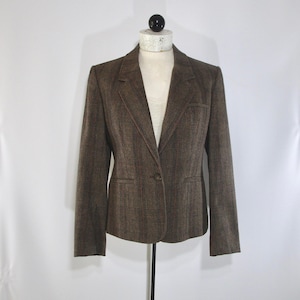 May include: A brown blazer with a plaid pattern, displayed on a mannequin. The blazer has a notched lapel, a single-button closure, and two front pockets. The fabric appears to be a woven material, and the overall style is classic and tailored.