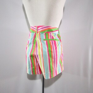 May include: Shorts with vertical stripes in bright colors of pink, green, orange, yellow, and blue. The shorts have a high waist and a back pocket with a green trim. The garment is displayed on a mannequin.
