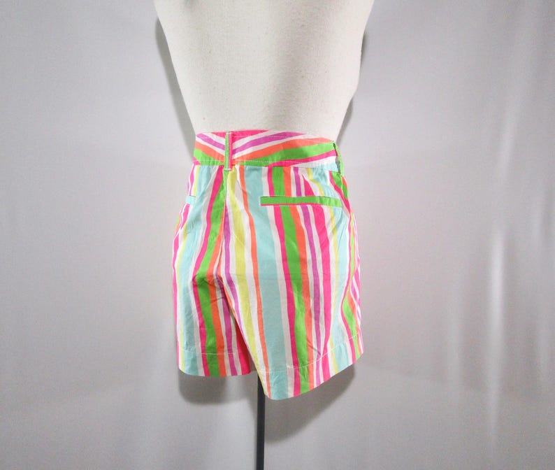 May include: Shorts with vertical stripes in bright colors of pink, green, orange, yellow, and blue. The shorts have a high waist and a back pocket with a green trim. The garment is displayed on a mannequin.