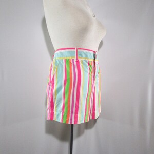 May include: A pair of colorful striped shorts in shades of pink, green, orange, and blue. The shorts have a waistband with a button closure and belt loops. The garment is displayed on a mannequin.