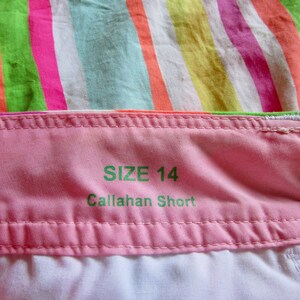 May include: Close-up of a pink fabric waistband with the text "SIZE 14 Callahan Short" in green. The background features colorful striped fabric in shades of pink, green, orange, and yellow.