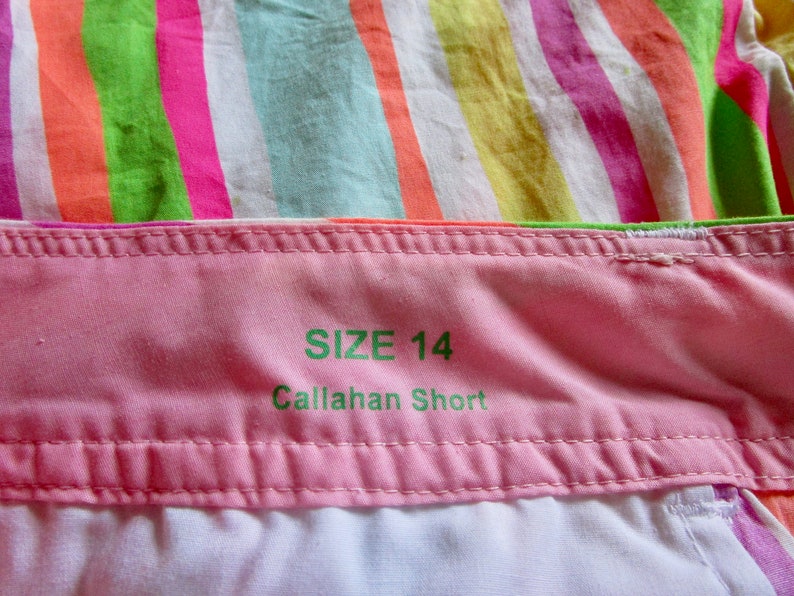 May include: Close-up of a pink fabric waistband with the text "SIZE 14 Callahan Short" in green. The background features colorful striped fabric in shades of pink, green, orange, and yellow.