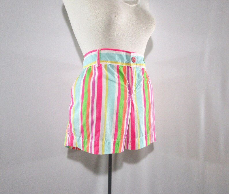 May include: Colorful striped shorts in shades of pink, green, blue, and white. The shorts have a button closure and belt loops. The vertical stripes create a vibrant and playful look, perfect for warm weather.