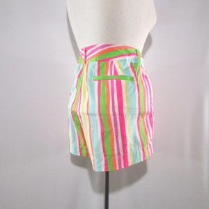 May include: Shorts with vertical stripes in bright colors, including pink, green, orange, and white. The shorts have a high waist and a small pocket on the back. The shorts are displayed on a mannequin.