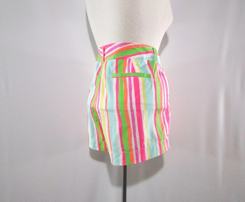 May include: Shorts with vertical stripes in bright colors, including pink, green, orange, and white. The shorts have a high waist and a small pocket on the back. The shorts are displayed on a mannequin.