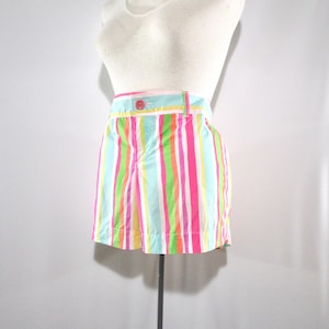May include: A pair of colorful striped shorts in a variety of bright colors, including pink, green, blue, and yellow. The shorts have a button and a belt loop. The garment is displayed on a mannequin.