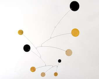 May include: A mobile sculpture featuring black and gold circles suspended from fine wires. The circles are balanced in mid-air, creating a dynamic and abstract design.