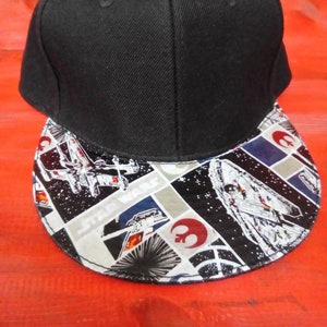 May include: A black and white Star Wars themed baseball cap with a black crown and a patterned brim. The brim features a collage of Star Wars characters and spaceships, including the Millennium Falcon, X-Wings, and Rebel Alliance symbols.