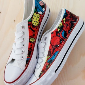 May include: A pair of white canvas shoes with a red, blue, and yellow comic book character print. The print features Iron Man, Spider-Man, and Captain America.