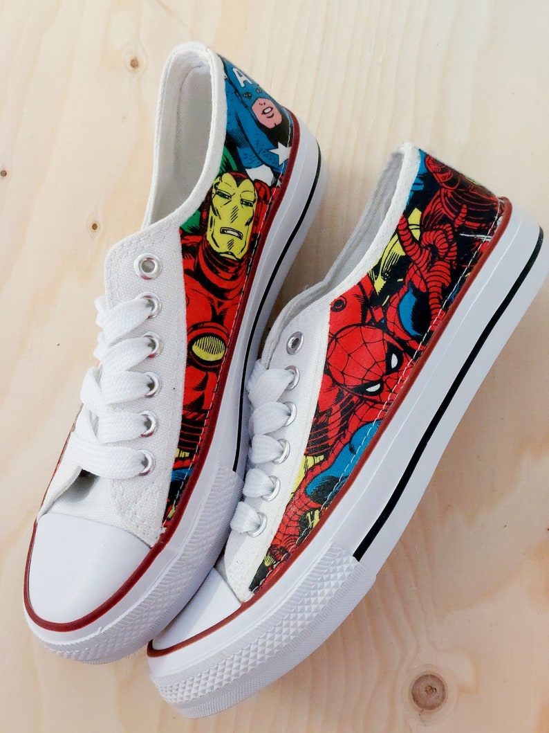 May include: A pair of white canvas shoes with a red, blue, and yellow comic book character print. The print features Iron Man, Spider-Man, and Captain America.