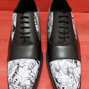 May include: Black leather oxford shoes with a white and black comic book print featuring Marvel characters Captain America and Iron Man.