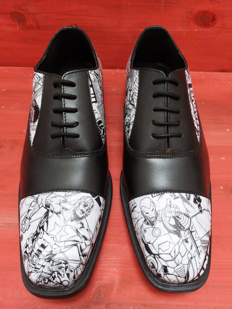 May include: Black leather oxford shoes with a white and black comic book print featuring Marvel characters Captain America and Iron Man.