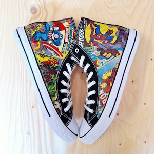 Può includere: Un paio di scarpe da ginnastica alte in tela nere con lacci bianchi e una stampa a fumetti con personaggi Marvel come Spider-Man, Capitan America e Iron Man.