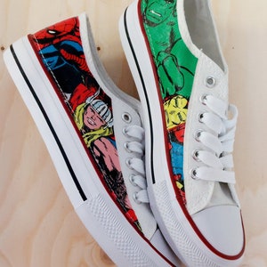 May include: A pair of white canvas shoes with a red, yellow, blue, green, and black comic book character print. The shoes have white laces and a red trim around the sole.