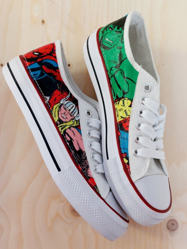May include: A pair of white canvas shoes with a red, yellow, blue, green, and black comic book character print. The shoes have white laces and a red trim around the sole.
