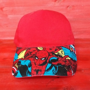 Può includere: Cappellino da baseball rosso con un design di personaggio dei fumetti con Spiderman sul davanti. Il design include uno schema di colori blu, rosso, giallo e nero.