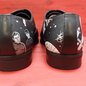 May include: A pair of black leather shoes with a white and black space-themed design. The shoes feature images of the Starship Enterprise, planets, and stars.