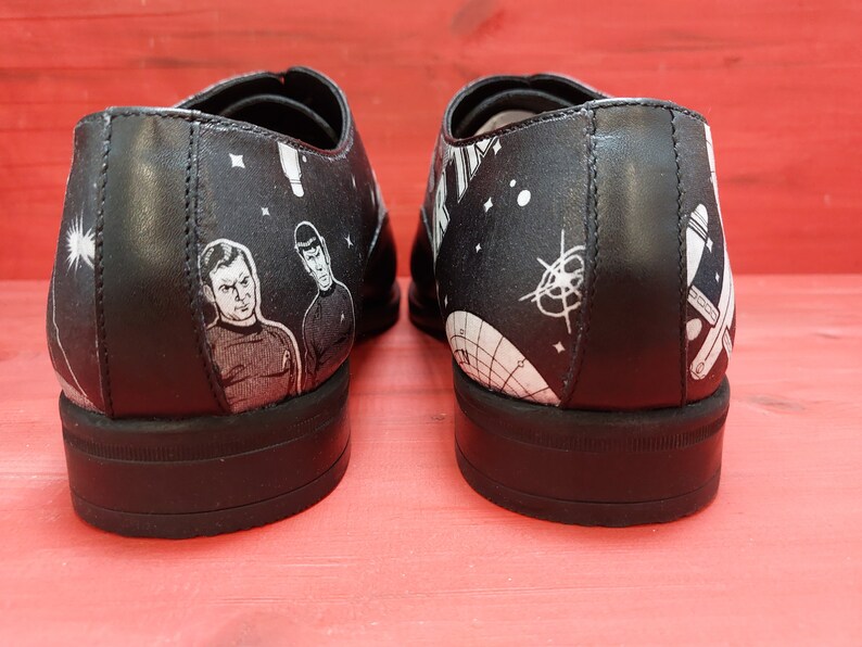 May include: A pair of black leather shoes with a white and black space-themed design. The shoes feature images of the Starship Enterprise, planets, and stars.